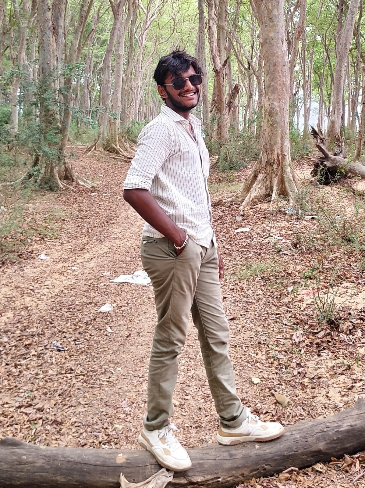 D Premsankar smiling in a forest, wearing sunglasses and a striped shirt
